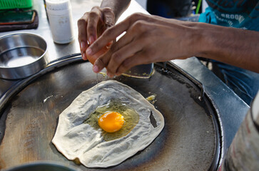 Roti with eggs being fried in a pan in the light of the sun.