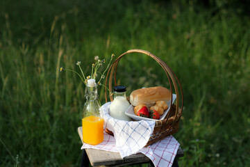 bread and milk in basket with bottle of orange juice on nature background