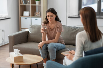 psychology, mental health and people concept - sad young woman patient with glass of water and woman psychologist at psychotherapy session