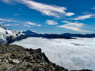 Sea of clouds hanging over the valley in front of Mount Cook, New Zealand. Rough gravel and stones in the foreground. 