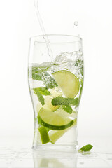 Clear shiny glass filled with lime and mint and delicious Mojito cocktail composed. Stream of water into a glass on white background.  Shallow depth of field