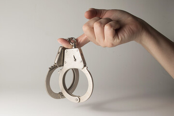 Metal handcuffs with a chain on a light background in a female hand