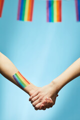 Closeup of young couple holding hands with rainbow flag in background