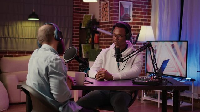 Internet radio host greeting guest doing fist bump hand gesture while recording podcast using digital video camera in home studio. African american podcaster in interview with famous influencer.