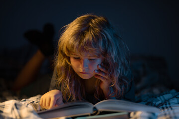 A little cute boy reading a book lying on the bed. Child reading a book on bedtime night. Kids...