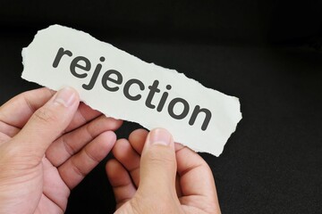 Hand holding a paper with written word rejection in black background. How to handle rejection concept.