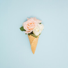 Ice cream cone with white and pastel pink roses and fresh green leaves. Summer minimal concept. Flat lay.