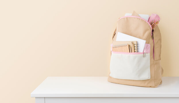 Stylish backpack with school stationery on table against beige background