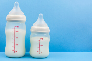 Two baby bottles with milk formula on a blue background. Feeding the baby. Space for the text.