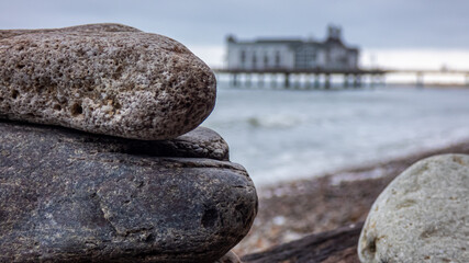 Fototapeta na wymiar Steinstapel fokussiert am Meer mit einer Seebrücke im unscharfen Hintergrund