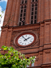 Fototapeta na wymiar Church clock. Red brick church tower with ancient black and white clock-face. Sunny day with blue sky and few clouds.