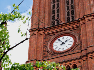 Church clock. Red brick church tower with ancient black and white clock-face. Sunny day with blue...