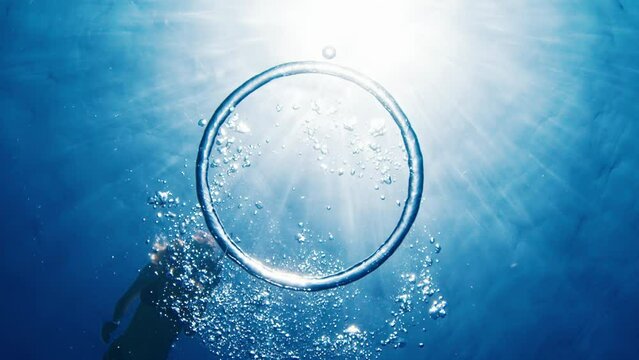 Woman swims in the sea and watches ring bubble moving underwater towards the surface