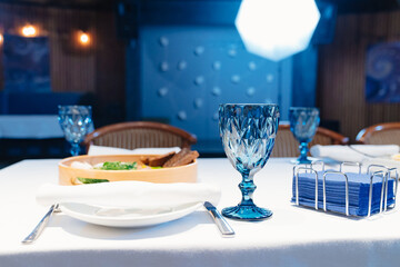white plate with napkin and cutlery, beautiful blue glass wine glass on table.