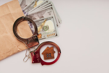 Envelope with dollars, wooden house and handcuffs on a white background. Bribe and financial fraud...