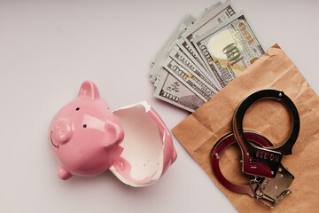 Bribe and financial fraud concept. Envelope with dollars, broken piggy bank and handcuffs on a table