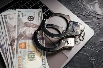 Handcuffs and dollar banknotes on a laptop keyboard. Online crime concept