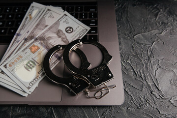 Handcuffs and dollar banknotes on a laptop keyboard. Online fraud concept