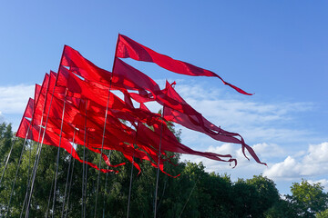 Red flags fluttering in the wind with blue sky and trees in the background