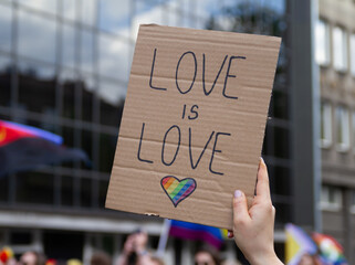 Hand holding placard sign Love is Love with rainbow flag heart, symbol of LGBT. Pride Parade, equality march to support and celebrate LGBT+, LGBTQ gay lesbian community.