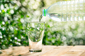 Pour water from a plastic bottle into a glass. The background of the plants in the garden.