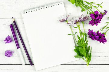 Naklejka premium Purple and white flowers of Osteospermum (Cape daisy) and a sketchbook (notepad) on a white background. Space for the text. Freelance, beauty business. Birthday, Mother's Day.