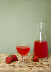 Strawberry drink in a glass on a wicker surface. Copyspace on a green background