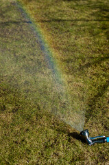 a water sprayer lies on the lawn and pours water over the grass creating a rainbow