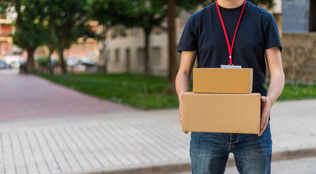 Fotograf&iacute;a de mensajero de medio cuerpo irreconocible, con cajas de cart&oacute;n, en una parcela. Fotograf&iacute;a en horizontal con espacio para texto.