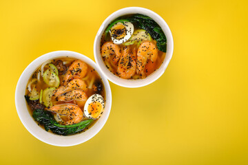 Two bowls with udon noodle soup with egg, shrimp and spinach