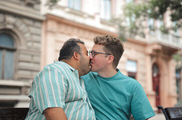 homosexual couple sitting on a bench are kissing