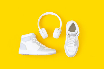 Sports shoes, sneakers and white headphones on yellow background. Music, audio books, learning...