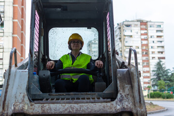 cheerful female excavator operator on construction site. Woman construction apprentice learning to...