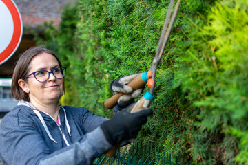 Cheerfully woman Cutting a hedge with clippers. Female gardener hedge trimming or rip bush with grass shears gardening scissors activity working during stay home at backyard.
