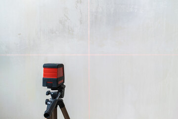 The laser level shows horizontal and vertical red light lines guides on a white textured background. Construction and repair tool.