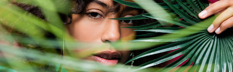 pretty african american woman looking at camera near exotic leaves on blurred foreground, banner.