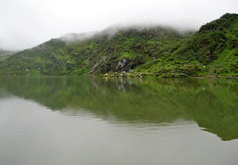 Fototapeta premium The verdant green terrain mirrored at Tsomgo Lake situated at 12,600 look mesmerizing in East Sikkim. This is a popular tourist spot of Sikkim. The terrain was covered with snow till April melted now.