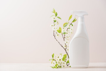 White bottle sprayer with cleaning liquid and blossoming tree branches on beige background....