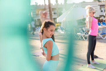 little girl doing sports exercises near hotel lounge chairs.