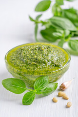 Traditional homemade italian pesto sauce made of blended fresh green basil leaves, pine nuts, garlic, Parmesan cheese and olive oil served in glass transparent bowl on white wooden background