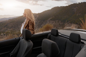 Side view of cheerful woman standing near convertible car looking away and smiling, travel concept