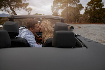 Happy man and woman sitting in convertible car outdoor and kissing, travel together, love concept