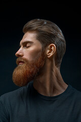 Perfect beard. the young man closed his eyes and turned his head in profile. Close-up portrait of young bearded man on black background