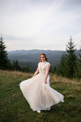 Fototapeta na wymiar Beautiful bride in a white wedding dress on a background of mountains.