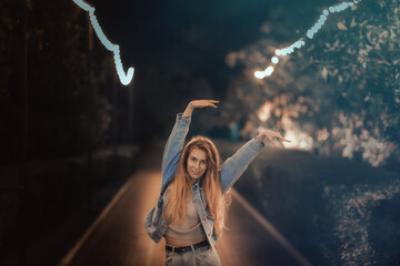A woman walks, waving her arms above her head, along a night alley in the park. Soft focus.
