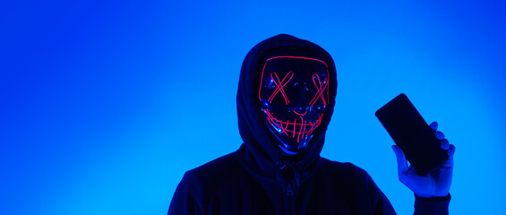 Anonymous hacker and face mask with smartphone in hand. Man in black hood shirt trying to hack...