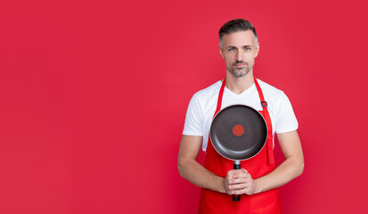 mature man chef in apron hold frying pan on red background