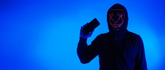 Anonymous hacker and face mask with smartphone in hand. Man in black hood shirt trying to hack...
