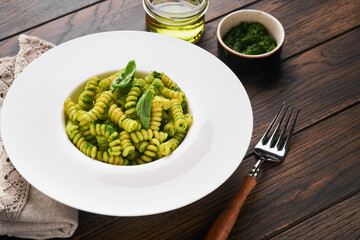 Italian Fusilli Pasta with Pesto. Fusilli pasta with basil pesto and herbs, parmesan cheese, basil and garlic on white plate on old wooden table background. Top view. Copy space. Mock up.