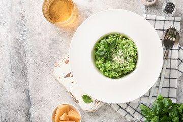 Italian risotto. Delicious risotto in white plate with pesto sauce or wild garlic pesto, basil, parmesan cheese and glass of white wine on old light grey table background. Top view with copy space.